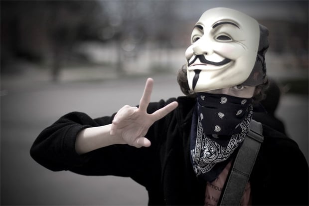 a hacker with an anonymous mask giving the peace sign
