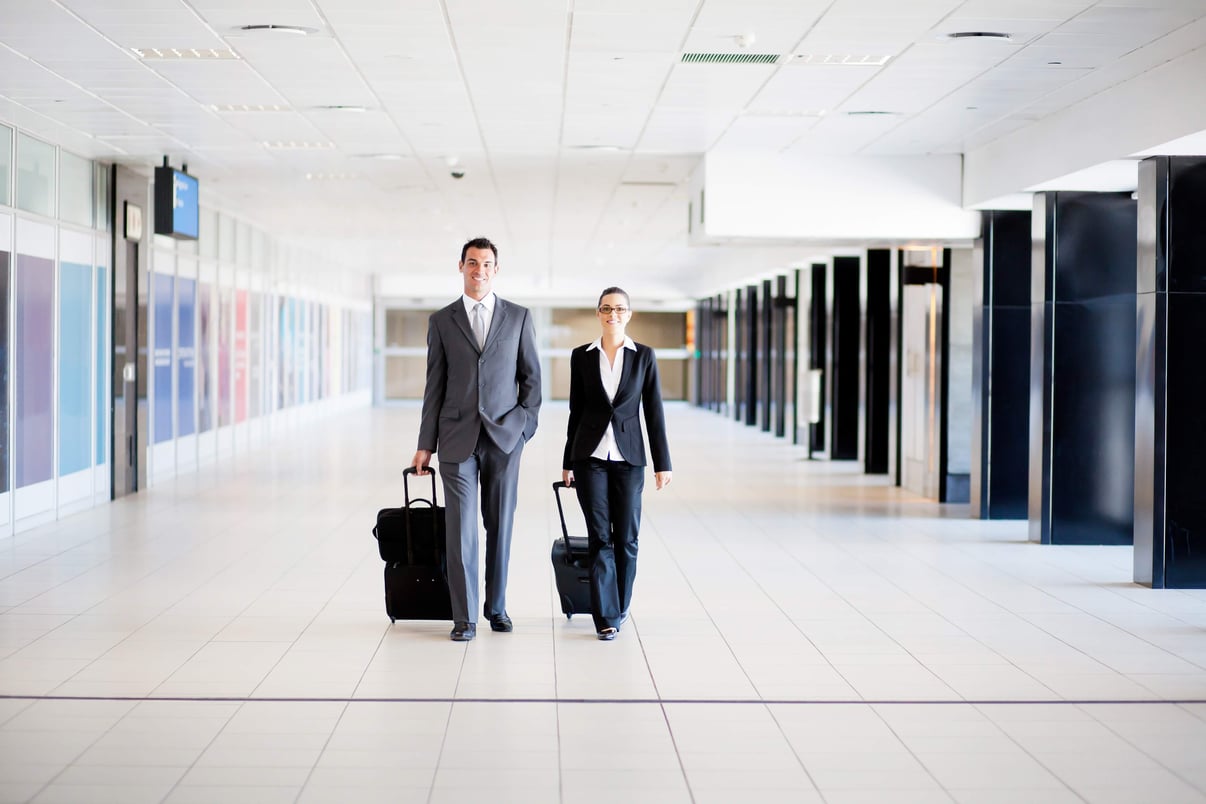 two professionals in suits walking an airport terminal with rolling suitcases