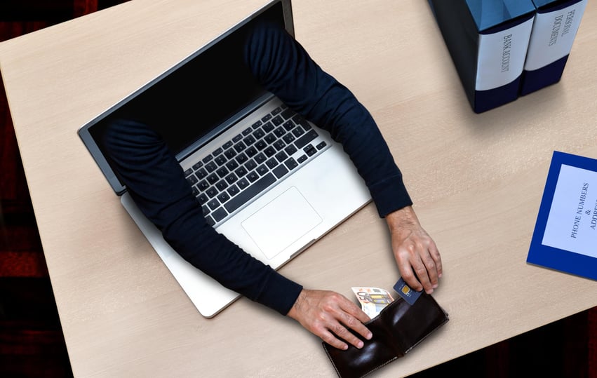 open laptop on a wood surface with black-sleeved arms pick-pocketing a wallet 