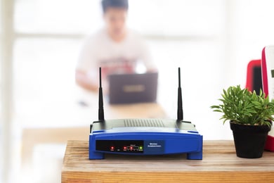 blue wifi router green plant on wood desk man using laptop rx