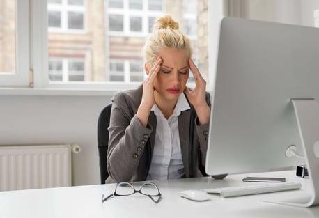 women holding her head at iMac on white desk