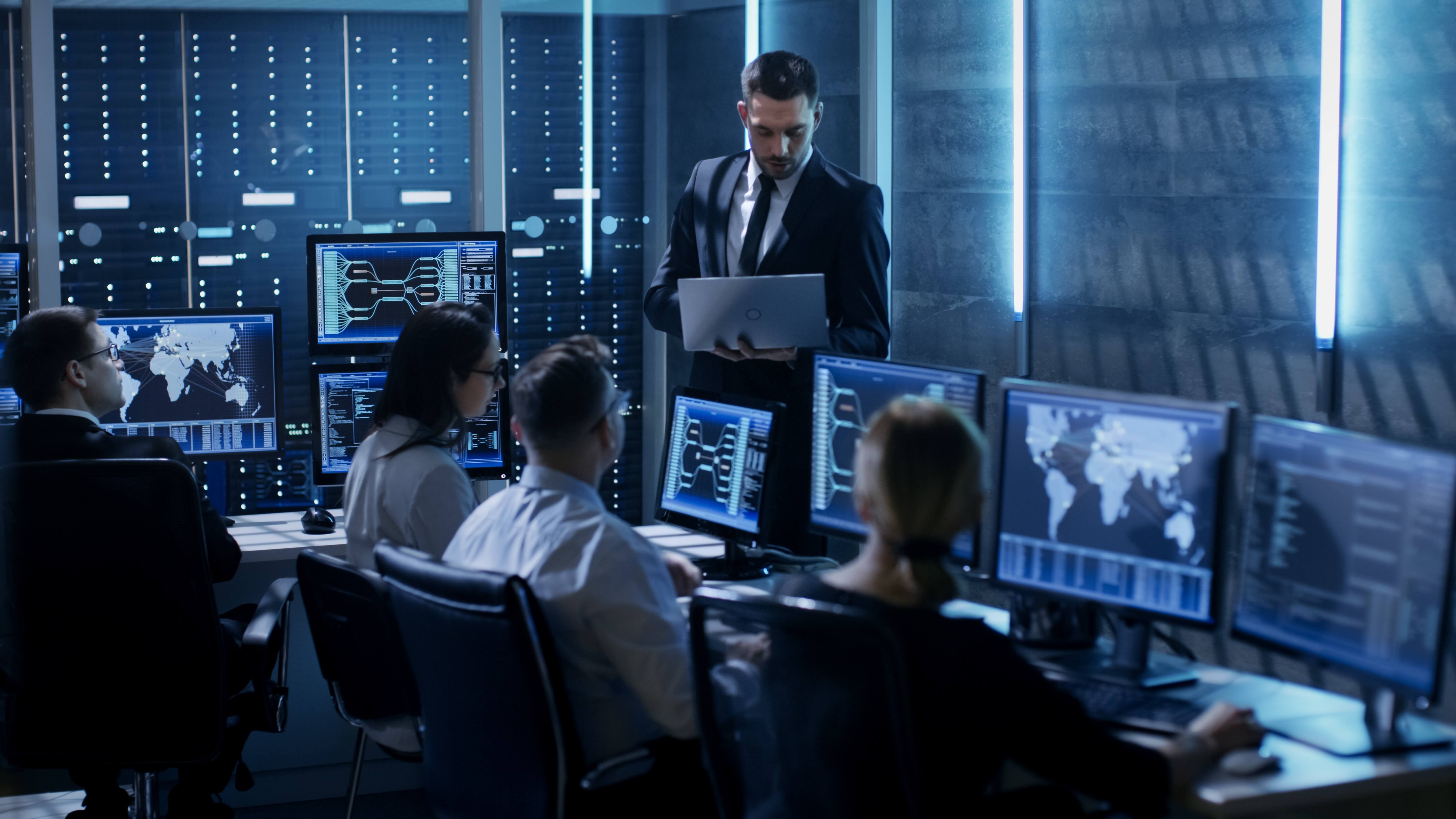 IT security pros in a dark blue room overlooking computers