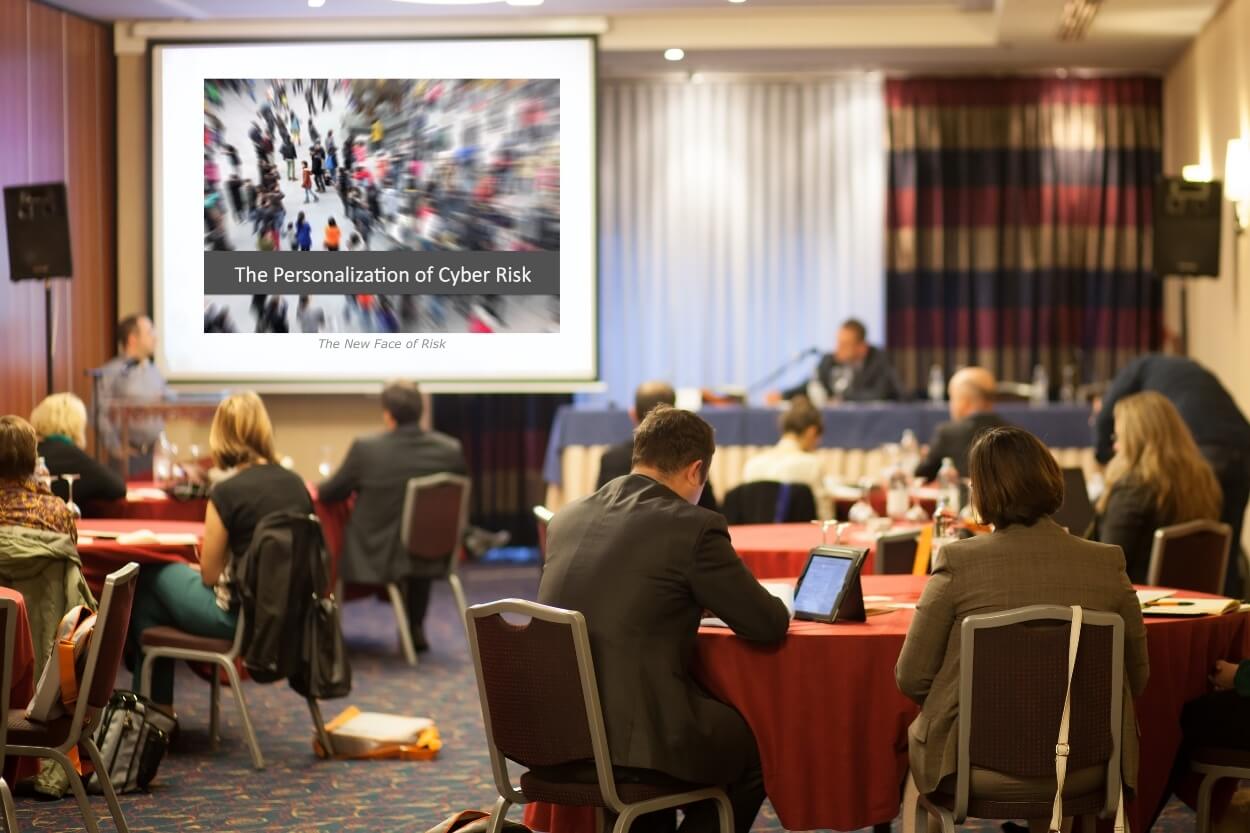 photo of a large conference room and presentation screen with red clothed circular tables and professionals at work with computers