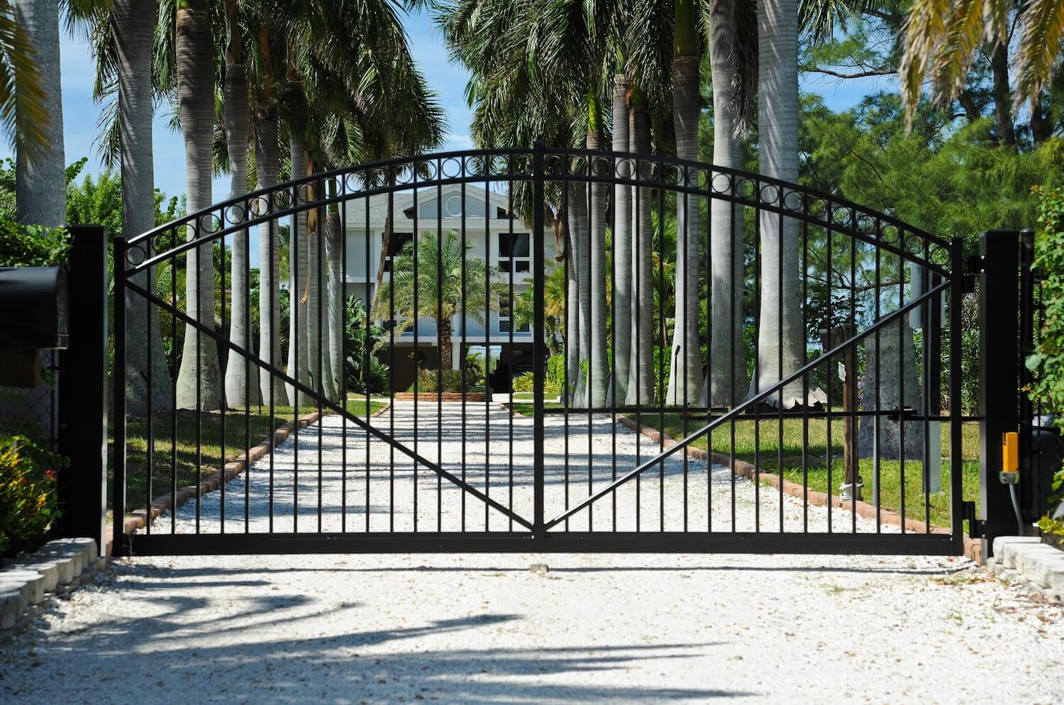 large black wrought iron gate at the entrance to a long driveway to a large house
