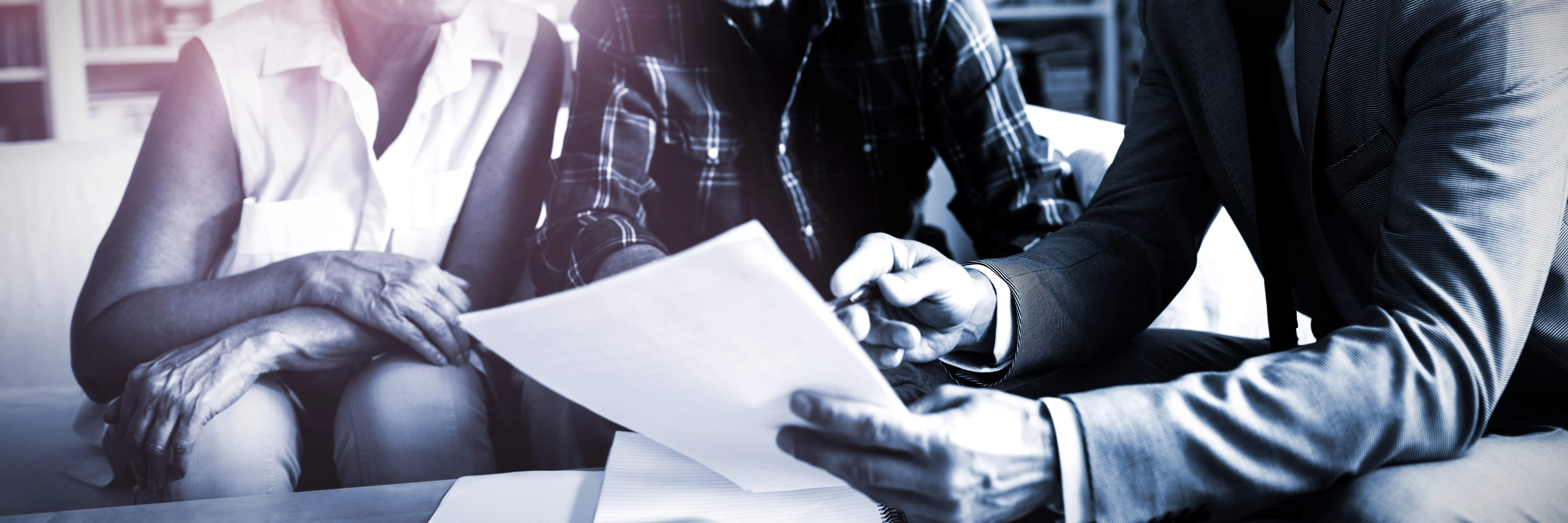 black and white image of man's hands holding a document with a pen as he reviews it with clients